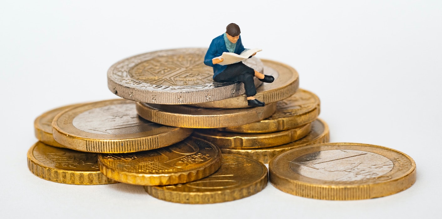 Small man sitting on pile of coins - article about how to get funding and investment for your small business
