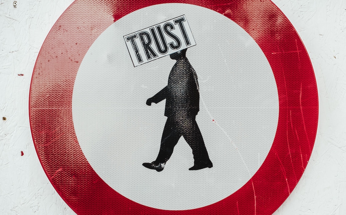 What Makes A Psychologically Safe Work Environment? Image of a roadsign with a man on white in a red circle, with TRUST written over the top