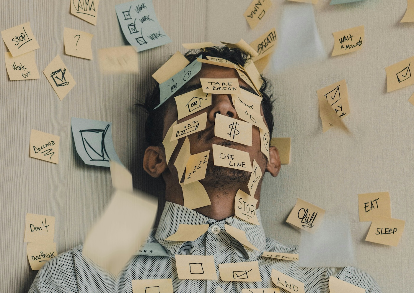 Time Management Tips for Small Business Owners: Navigating Through the Year. Image of a man with dark hair and a blue shirt laying down with post-its all over him with frantic notes around tasks to do and being busy.