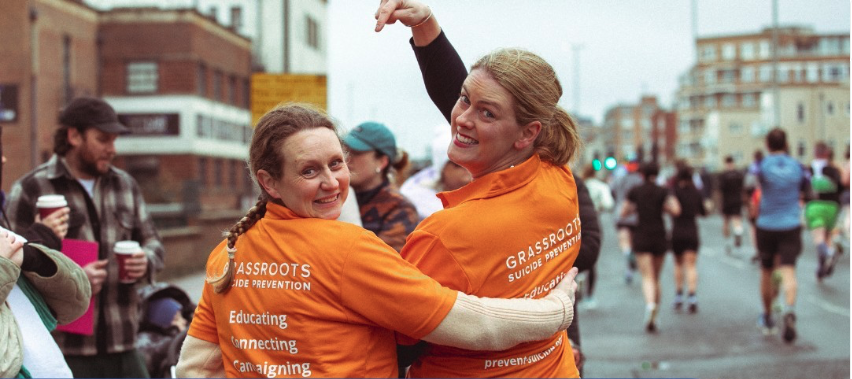 Finding the Right Charity Trustee Role blog post image showing two women smiling and wearing orange Grassroots Suicide Prevention t-shirts at the Brighton Marathon.